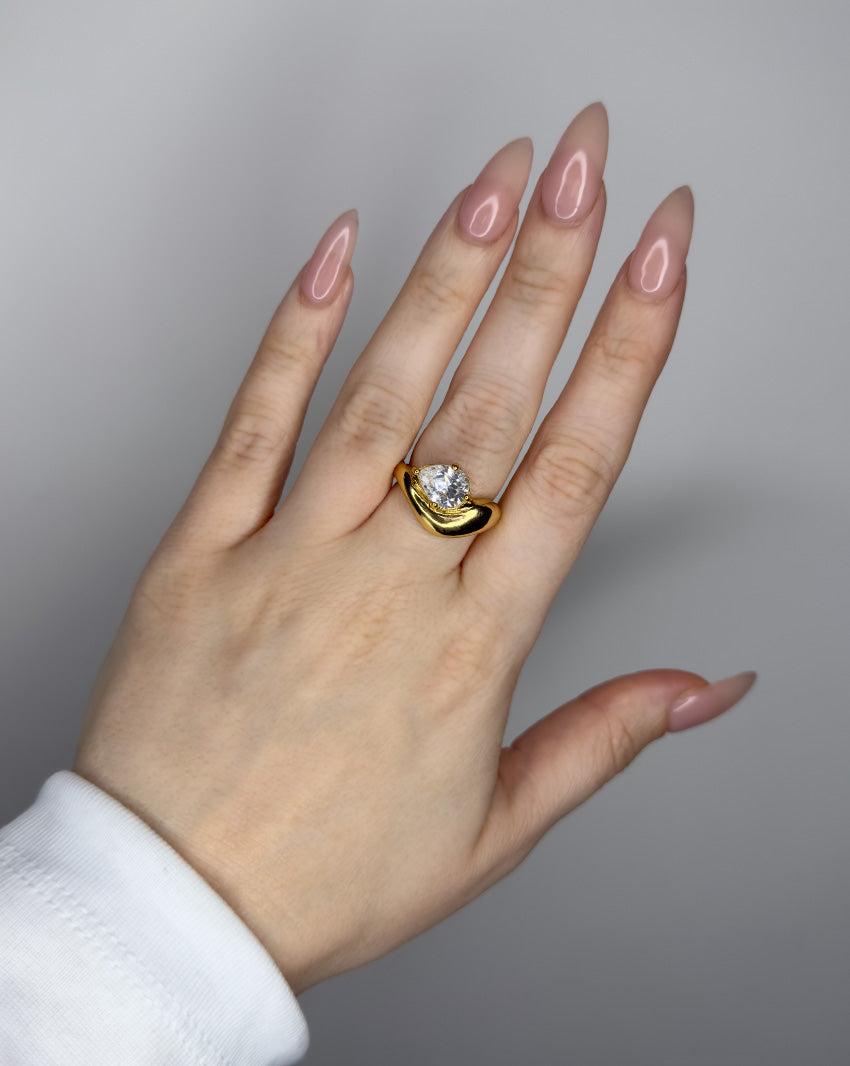 Liquid ring design with pear shape imitation diamond. 14k gold plate over recycled brass.