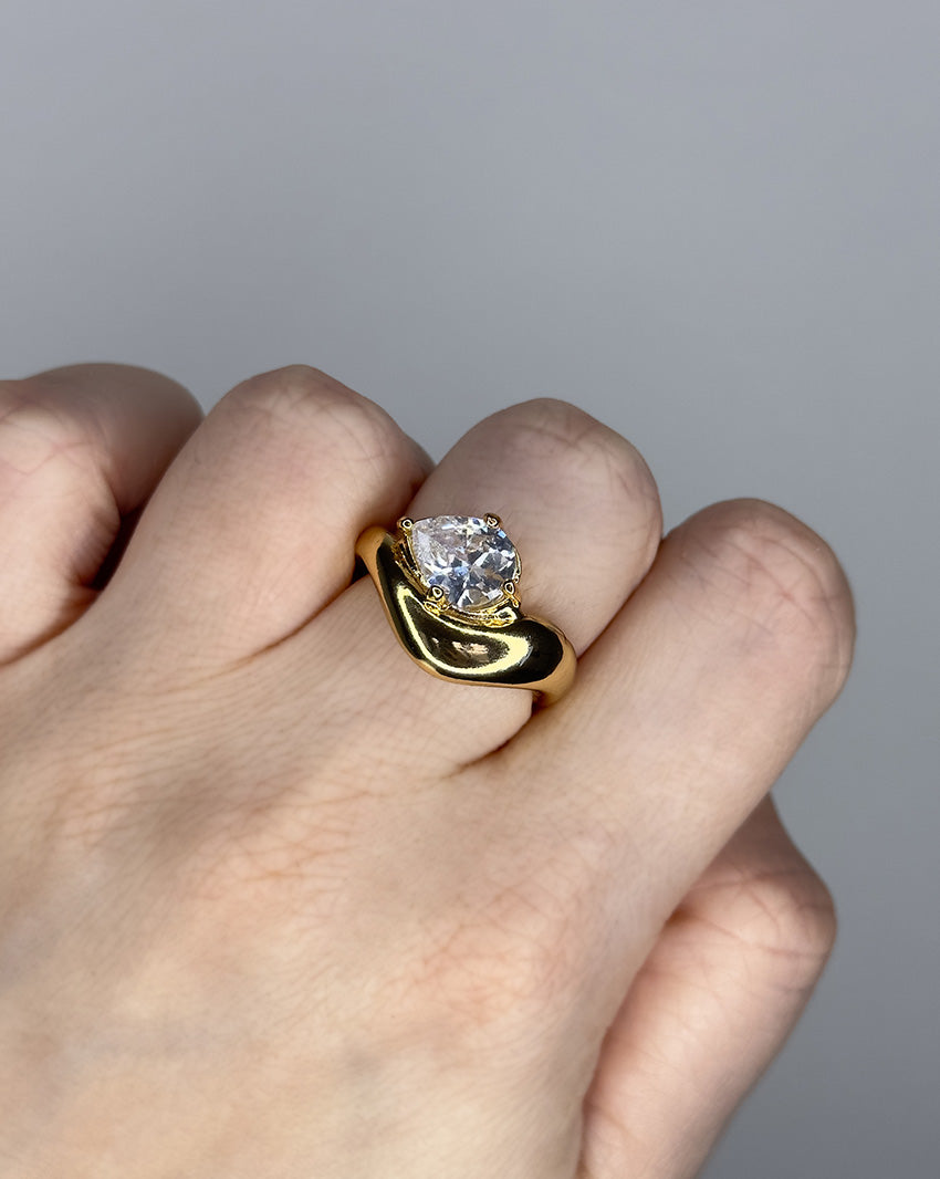 Liquid ring design with pear shape imitation diamond. 14k gold plate over recycled brass.
