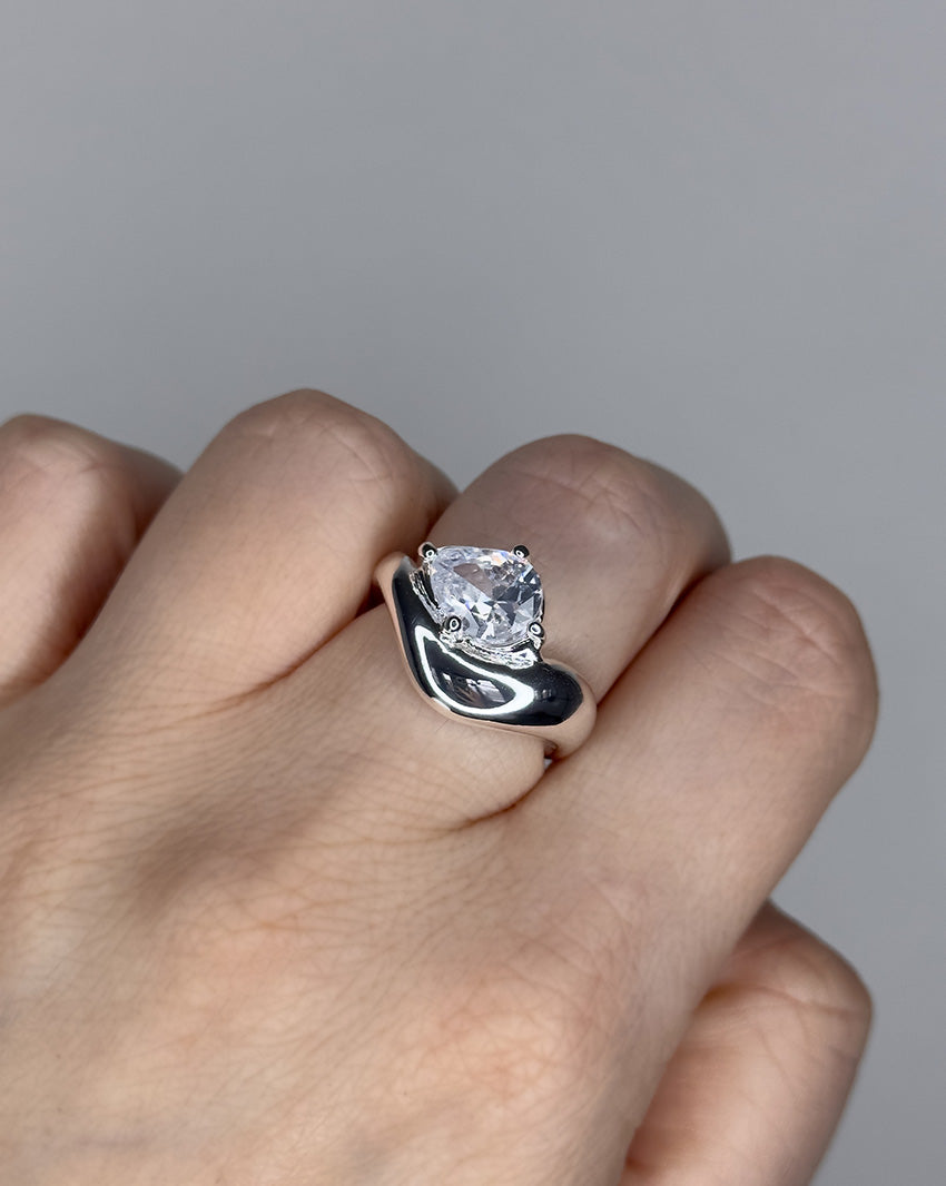Liquid ring design with pear shape imitation diamond. Sterling silver plate over recycled brass.